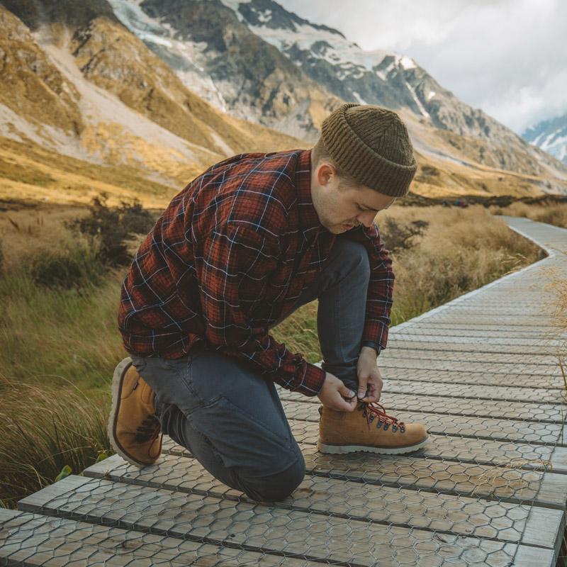 A man wearing Adventure Pants tying his shoes on a wooden pathway in the mountains.