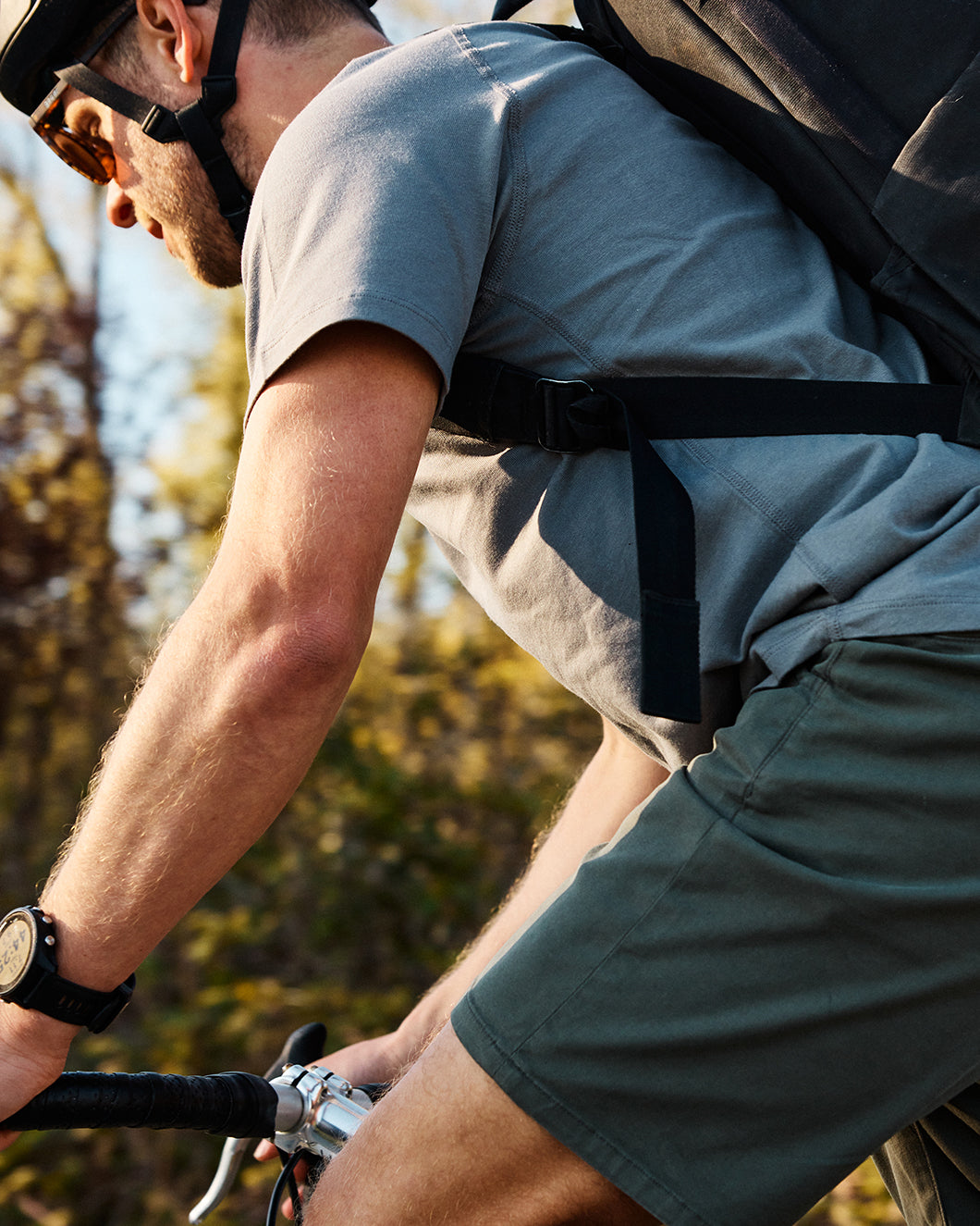 A person wearing a helmet, sunglasses, a gray t-shirt, and green shorts rides a bicycle outdoors on a sunny day.