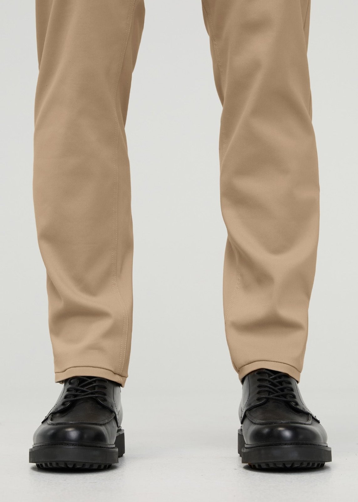 Khaki tapered trousers with visible center seams, cuffed at ankles, worn with black lace-up shoes.