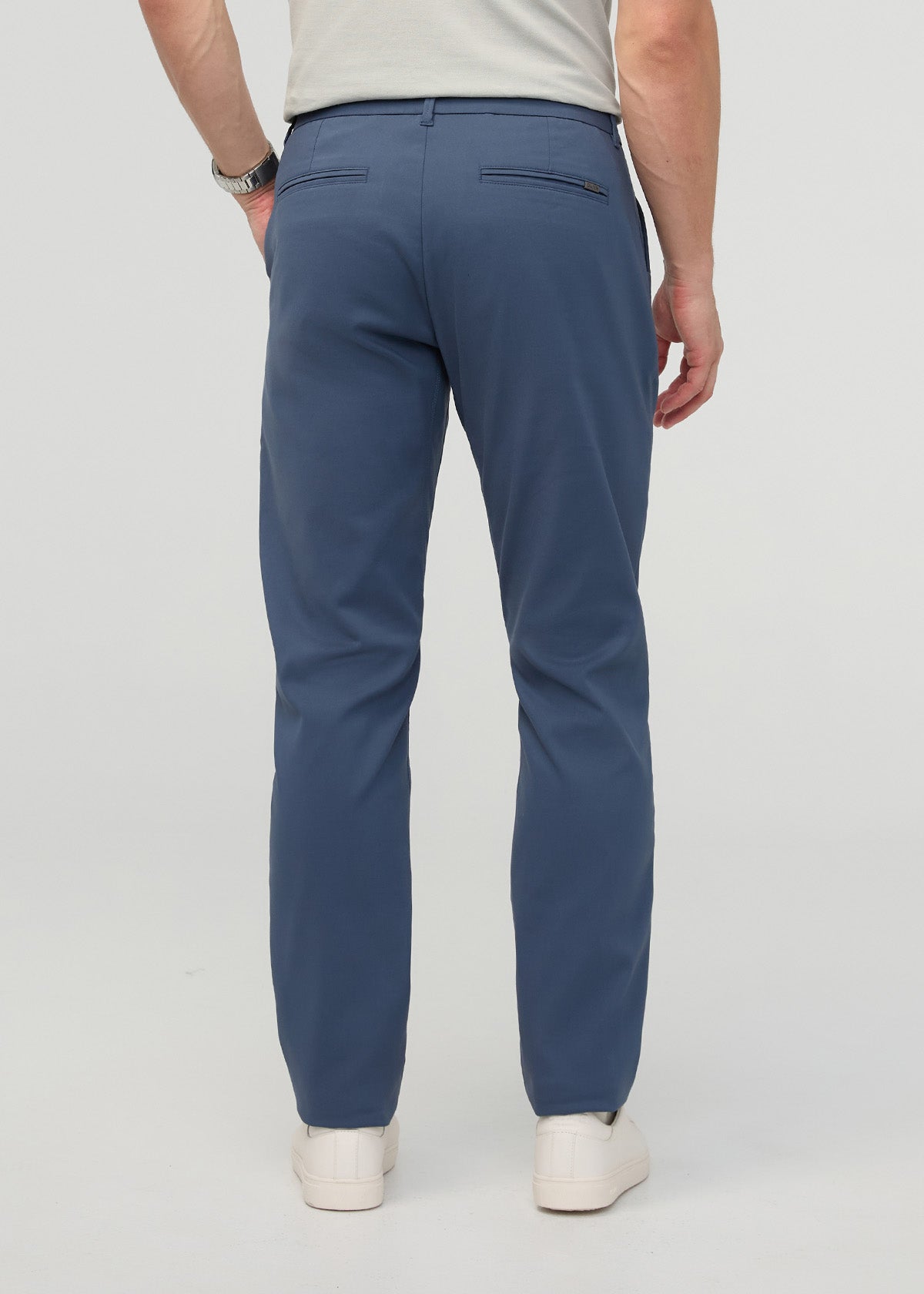 Man wearing heritage blue relaxed taper trousers with cream shirt, shown from back view with hands in pockets.