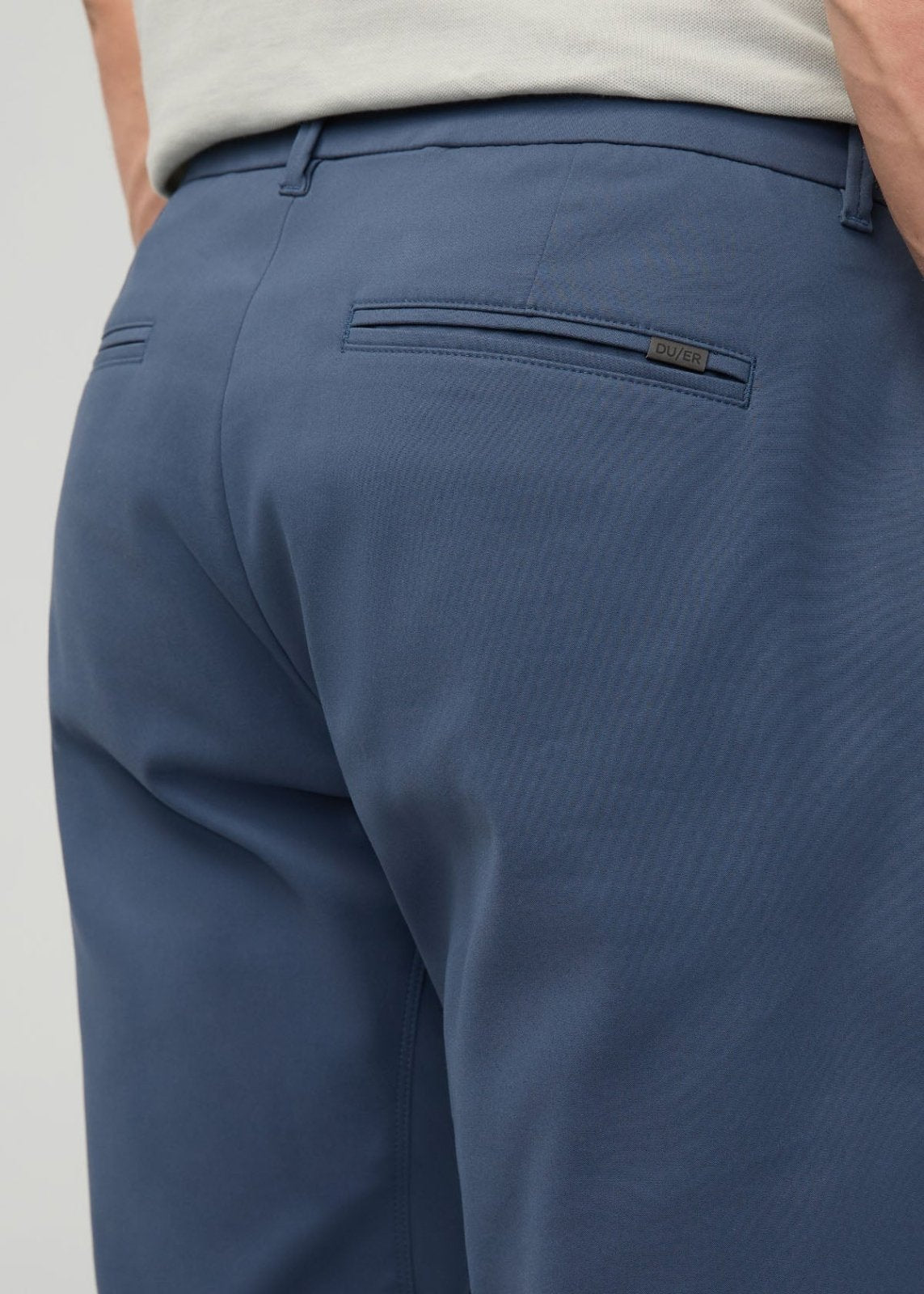 Blue tapered trousers with back pocket and brand label, worn with cream colored shirt.