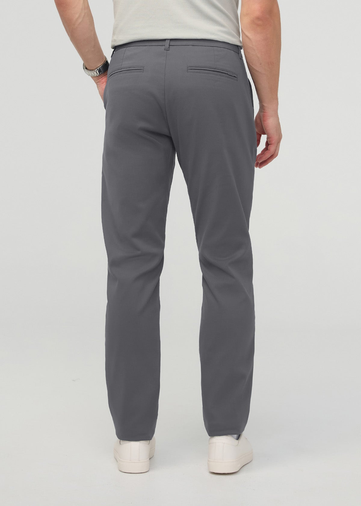 Gray relaxed taper trousers with back pockets, shown on model from behind wearing cream sneakers.