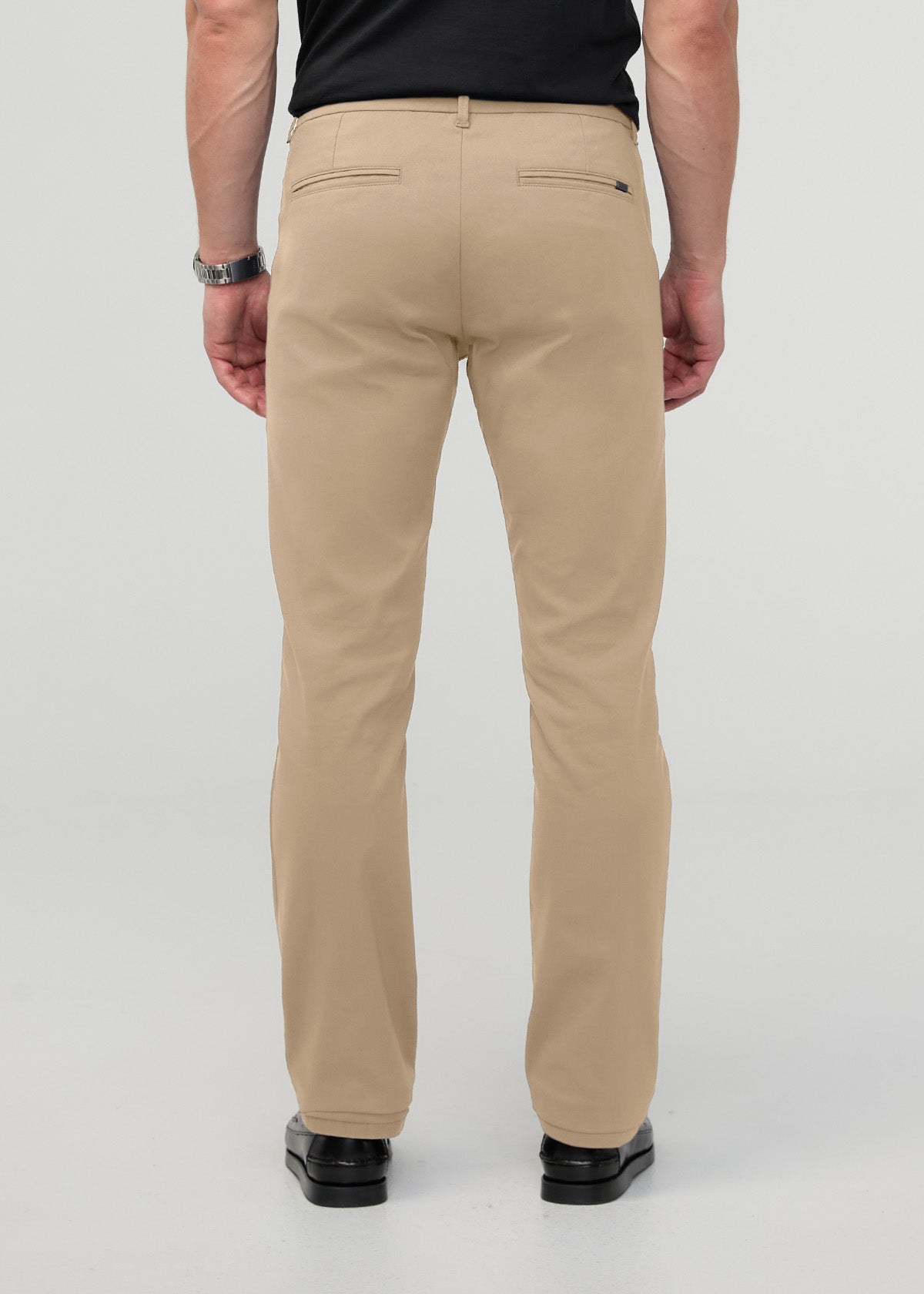 Beige straight-leg trouser with back welt pockets and belt loops, shown from rear view on model wearing black shirt.