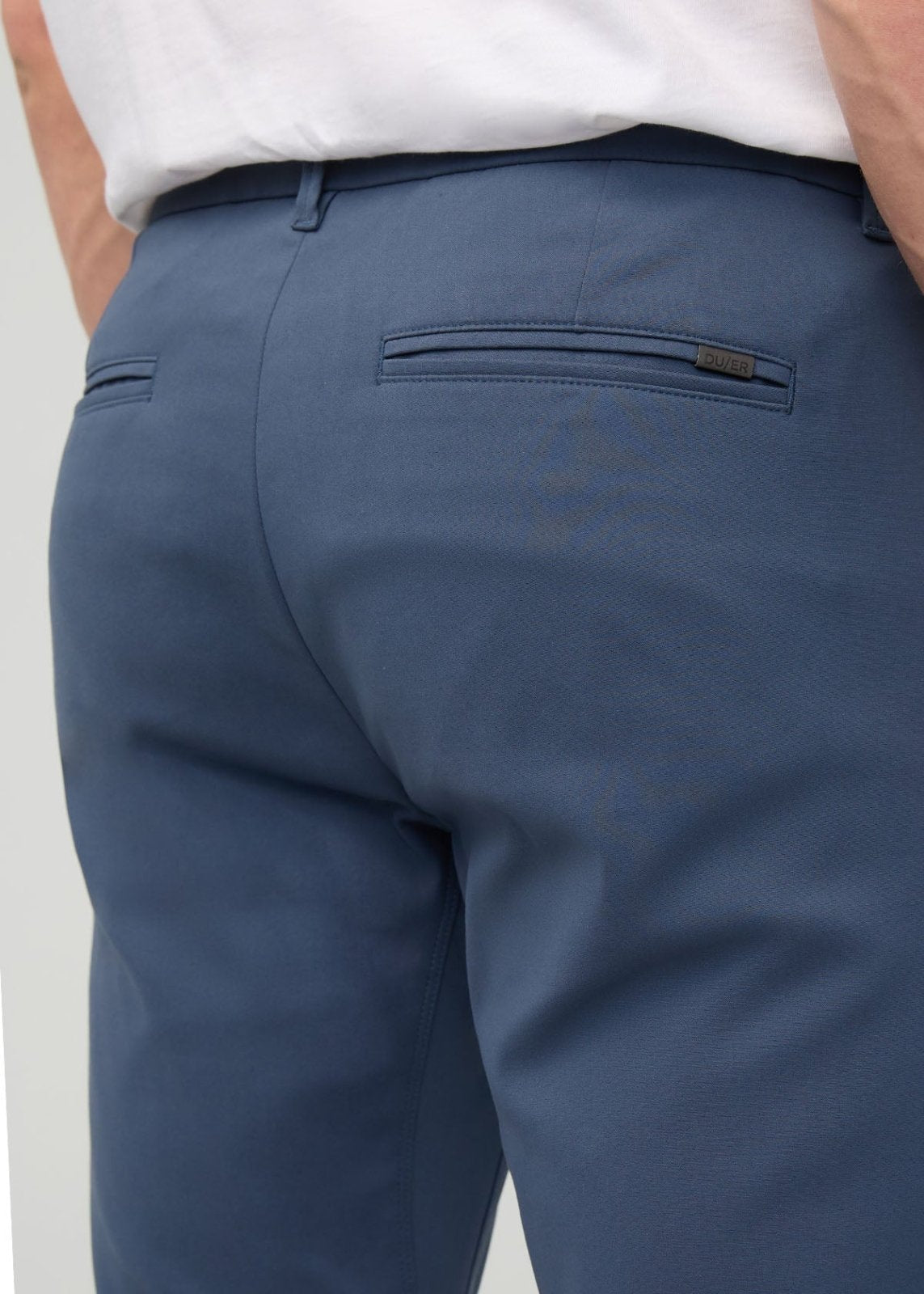 Blue slim straight trousers with back pocket detail, worn with white shirt.