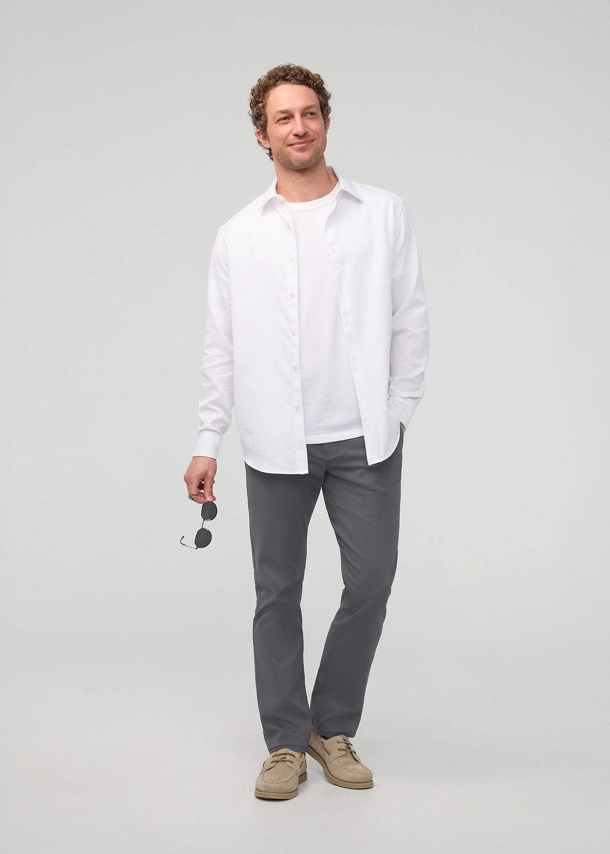 Man wearing river rock gray slim straight trousers with white button-up shirt and tan boat shoes.