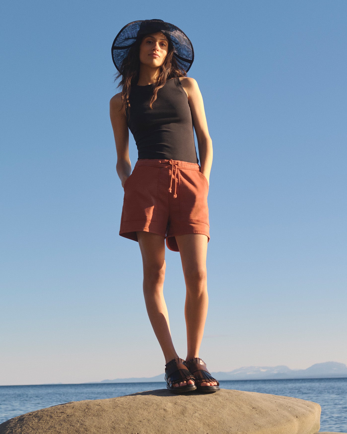 woman standing on rock overlooking ocean wearing DUER shorts 