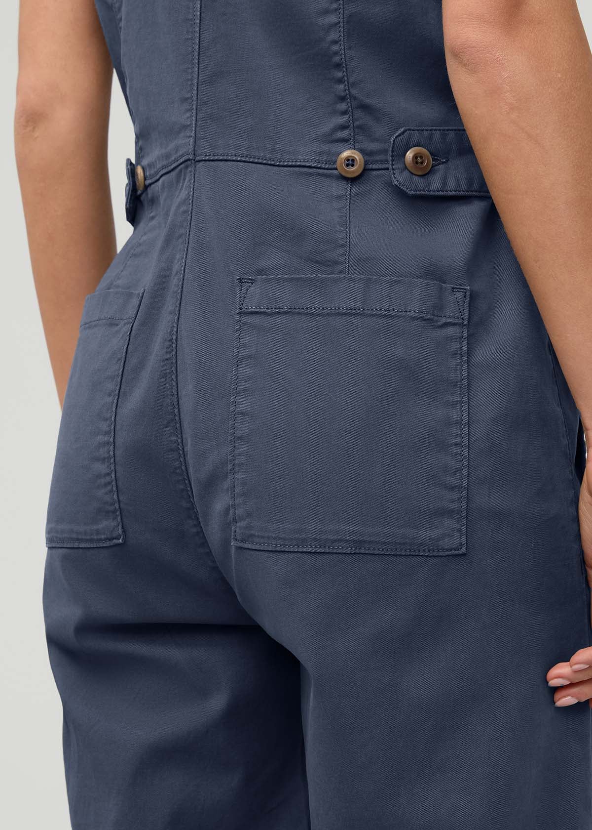 Heritage blue sleeveless boiler suit with cargo pockets, wooden buttons, and adjustable waist tabs shown on model from waist 