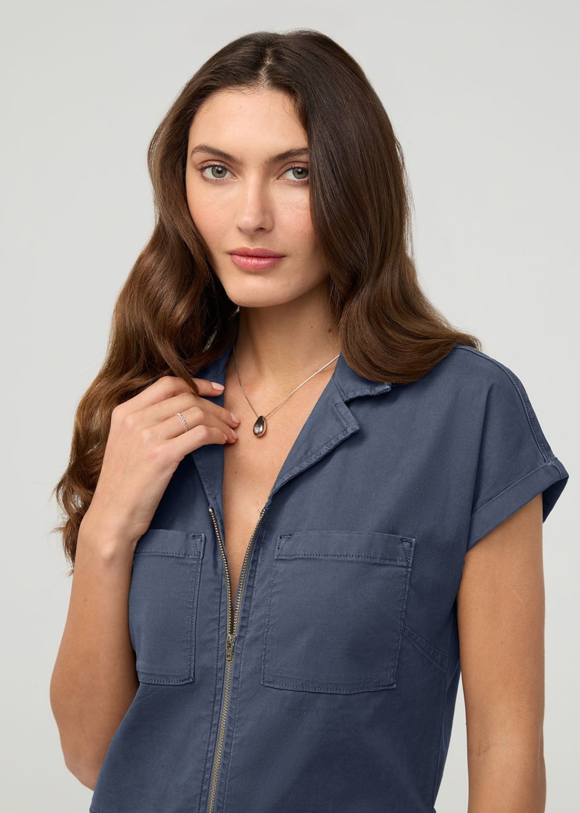 Woman wearing a heritage blue short-sleeved boiler suit with front zip closure and chest pockets.