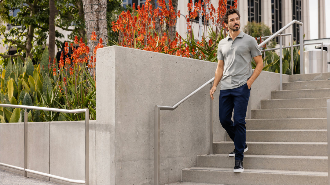 A man wearing a light gray polo shirt and navy pants, walks down concrete steps. 