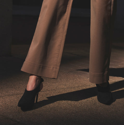 a woman in high heels wearing brown pants standing on a sidewalk